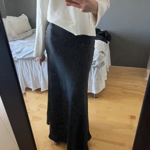 Svart satinkjol från AWARE - Supersnygg svart långkjol från AWARE i glansigt satinmaterial. Kjolen har en rak passform med resår i midjan. Är 170 cm lång för referens. Säljer då den aldrig kommit till användning🙈🙌🏻