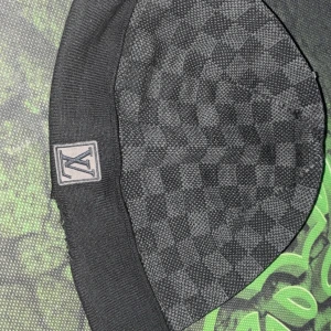 Louis Vuitton svart rutig mössa - Snygg svart mössa från Louis Vuitton med klassiskt rutigt mönster och LV-logga framtill. Mössan är stickad och har en ribbad kant för extra komfort. Perfekt accessoar för att lyfta din streetstyle under kyliga dagar. Den är lite paj men syns ej när man har på sig den.