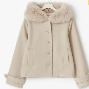 Slutsåld!!!Använd få gånger! Beige kappa med fuskpäls-krage - Snygg beige kappa med fluffig fuskpäls-krage och knappar framtill. Jackan har raka ärmar med knappdetalj vid ärmslut och två fickor fram. Perfekt för dig som vill ha en stilren och mysig look under kyliga dagar.