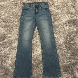 Blå bootcut jeans från Kappahl 158 - Snygga blå jeans från Kappahl i storlek 158 med klassisk bootcut passform. Jeansen har en ljus tvätt och kontrastsömmar. Perfekt för dig som gillar bootcut stilen.
