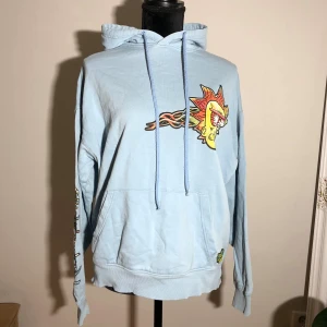 Rick and Morty hoodie från Pull&Bear - Ljusblå hoodie från Pull&Bear x Rick and Morty med stora tryck. Längd ca 70cm. Ärmlängd ca 60cm. Pris: 10kr