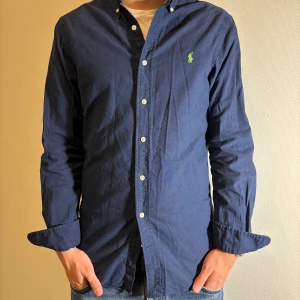 Ralph Lauren Skjorta - Säljer denna snygga marinblå skjorta från Ralph Lauren i slim fit-modell. Skjortan har en snygg neongrön logga på brösten. Skjortan är använd sparsamt och saknar defekter. Modellen är 181cm och väger 72kg.  Tveka inte vid frågor eller prisförslag🤝✍️!