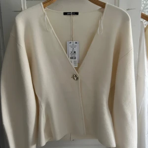 Beige kofta från Gina Tricot - Superfin beige kofta från Gina Tricot med v-ringning och en snygg guldig knapp framtill. Aldrig använd och prislapp sitter kvar