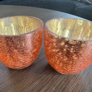 Ljyslyktor i rosa/guld - Bilderna visar två dekorativa glaslyktor i rosa/kopparfärgat glas med guldinsida. De har en vacker krackelerad yta och passar perfekt som värmeljushållare eller dekoration. Inga synliga sprickor eller större skador, endast mindre bruksspår. Säljes i par.