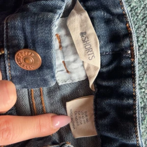 Blå jeansshorts med dragkedjor - Snygga blå jeansshorts med klassisk femficksdesign och coola dragkedjor på fickorna framtill. Shortsen har bälteshällor, knappstängning och är tillverkade i mjuk bomullsdenim. Perfekta för varma dagar och en avslappnad stil.