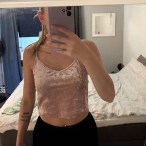 Linne - Säljer en ljusrosa croppad linne i mjuk sammet med tunna axelband och v-ringad hals. Linnet har en glansig finish som ger en lyxig känsla och passar perfekt till både jeans och kjol. Enkel och stilren design som är lätt att matcha.