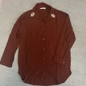 Vinröd skjorta  - Vinröd skjorta med pärldetaljer vid kragen. (Ser mer brun ut på bild än verkligheten). 