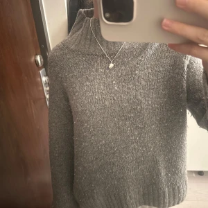 Grå stickad tröja från H&M - Mysig grå stickad tröja från H&M med hög krage och breda ärmar. Tröjan är ribbstickad nertill och vid ärmslut. Storlek xs