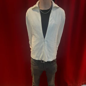 Vit zip-kofta med krage från hm - Säljer en stilren vit kofta med dragkedja och klassisk krage. Perfekt att slänga på över en t-shirt för en clean look. Materialet känns lätt och skönt mot huden, och passformen är normal. Enkel att matcha med jeans eller chinos.