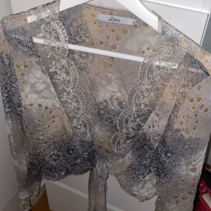 Spetsig topp/blus - Superfin transparent blus  i beige och gråblå toner med blommigt mönster, spetsdetaljer och  glitter ✨Knyt fram för en feminin och elegant look, perfekt över ett linne eller klänning. I mycket fint skick! Storlek XL, men tajt i bland annat armarna så passar L.