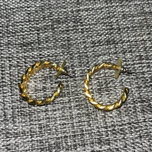 Två par guldiga örhängen - Säljer två par snygga örhängen i guldton. Ett par är halvcirkelformade med tvinnad design, det andra har en chunky kedjelänk-look. Båda har klassiska pluppar i plast för enkel användning. Perfekt för dig som gillar statement-accessoarer.