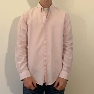 Ljusrosa skjorta från Zara Man - Snygg ljusrosa skjorta från Zara Man i slim fit-modell. Skjortan har klassisk button down-krage, långa ärmar och knäppning framtill. Tillverkad av bomull. Modellen är 180 cm lång (har vanligt viss S/M i storlek)