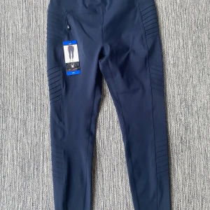 Mörkblå leggings från Spyder Active - Snygga mörkblå leggings från Spyder Active med coola ribbade detaljer längs benen. De har en hög midja och är gjorda i stretchigt syntetmaterial som passar perfekt för träning. Diskret logga med spindel på baksidan ger extra stilpoäng. Mått Midjan: ca 37 cm Längd från grenen och ner: ca 64  77% polyester och 23% elastan  Kommer från ett djur och rökfritt hem.