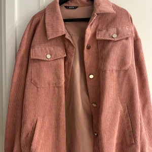 Rosa manchesterjacka från SHEIN - Snygg rosa manchesterjacka från SHEIN med oversized passform. Jackan har klassisk krage, två stora bröstfickor med knappar och sidofickor. Tydlig ribbad struktur och silvriga knappar framtill ger en cool och trendig look.