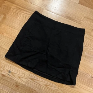 Svart kortkjol i linne - Enkel svart kortkjol i linne med rak passform och diskret slits framtill och dragkedja i bak. Endast använd 1 gång.