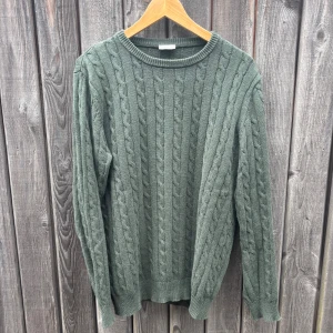 Grön stickad tröja från John Henric - Snygg grön stickad tröja från John Henric i storlek M. Tröjan har ett klassiskt kabelstickat mönster, rund hals och långa ärmar. Perfekt för dig som gillar en chill och stilren look med lite struktur i materialet.