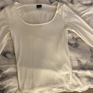 Vit långärmad topp från Gina Tricot - Säljer en stilren vit långärmad topp från Gina Tricot i storlek XS. Toppen har en djup rundad halsringning och är gjord i mjukt, stretchigt material som sitter snyggt mot kroppen. Perfekt att matcha med jeans eller kjol för en clean look. Dock några små fläckar men inget man tänker på 
