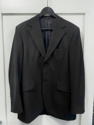 Svart Kavaj från Tiger of Sweden - Stilren svart kavaj från Tiger of Sweden med klassisk passform, två knappar framtill och tre fickor. Fodrad insida i blankt material och diskreta knappar vid ärmslut. Perfekt för dig som vill ha en tidlös och snygg look. Det står ingen storlek på insidan men jag har vanligtvis M och den är för stor så gissar på L.