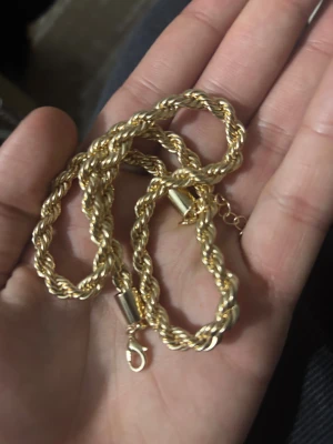 Guldtonat tvinnat halsband - Snyggt halsband med tvinnad kedja i guldtonad metall. Kedjan har en robust karbinhake och förlängningskedja för justerbar längd. Perfekt för dig som gillar klassiska och stilrena smycken med lite extra edge.