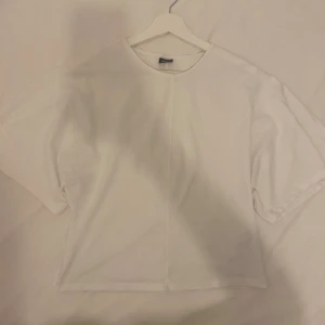 Vit tight t-shirt från Gina Tricot - Säljer en vit t-shirt från Gina Tricot i storlek L. Modellen är tight i midjan och loose vid armarna. korta ärmar och rund halsringning. Materialet är mjuk bomull och t-shirten har en enkel, clean look utan mönster eller detaljer. Perfekt för en chill och avslappnad stil.