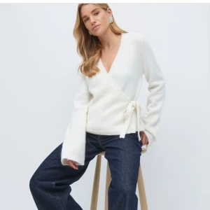 Vit omlottkofta med knyt - Superfin vit omlottkofta med knyt i sidan och v-ringad hals. Koftan har långa ärmar och är stickad i ett mjukt material som känns både lyxigt och bekvämt. Perfekt att styla med jeans eller kjol för en clean look. PRISET KAN DISKUTERAS 💕