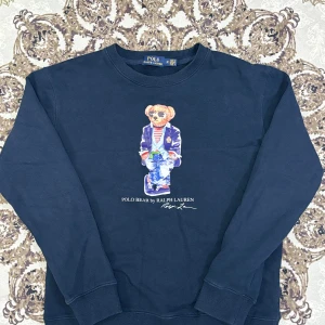 Polo Ralph Lauren Polo Bear Sweatshirt - Snygg och klassisk sweatshirt i marinblått med den ikoniska Polo Bear trycket på framsidan. Tröjan är i mjukt och bekvämt material och passar perfekt både till vardags och vid mer avslappnade tillfällen.  Längd från axeln och ner: 59 cm Bredd under armhålorna: 51 cm  📦 Skickas snabbt & välpackat.