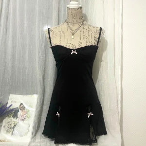 Svart kort klänning med spets och rosetter - Supersöt svart kort klänning med hjärtformade spetsöppningar och volangkant upptill. Passar storlek XS-S (34-36). Dockan är i storlek 36.