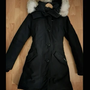 Svart Canada goose jacka  - Svart Rossclair Parka från Canada Goose med lång passform, sitter bra, med knappar framtill och huva med fluffig päls.