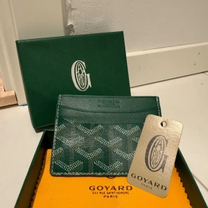 Plånbok  - Snygg grön plånbok  med klassiskt grafiskt mönster i vitt och grått. Slimmad design med flera fack för kort och sedlar. Perfekt för dig som gillar lyxiga accessoarer.