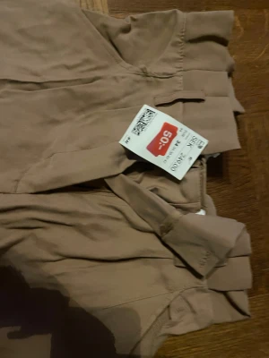 Beige kostymbyxor från H&M, strl 34 - Snygga beige kostymbyxor från H&M i storlek 34. Byxorna har hög midja och ett klassiskt rakt snitt med bälteshällor och dold dragkedja framtill. Perfekt för en clean och stilren look. Materialet är mjukt och har en lätt struktur.