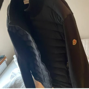 Svart moncler cardigan - Säljer en svart cardigan  från Moncler med quiltad framsida och ärmar. Jackan har dragkedja och Moncler-logga på ärmen. Materialet är dunfyllt och polyester, perfekt för kyliga dagar. Stilren och snygg design som funkar till många outfits. Stl xl sitter perfekt för L