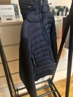 Mörkblå Moncler cardigan  med huva - Snygg mörkblå cardigan från Moncler med stickade ärmar och detaljer. Jackan har huva med snörning, dragkedja framtill och en ficka med zip på ärmen. Perfekt för dig som vill ha en stilren och exklusiv look med coola materialmixar. Kan gå ner i pris vid snabb affär!!