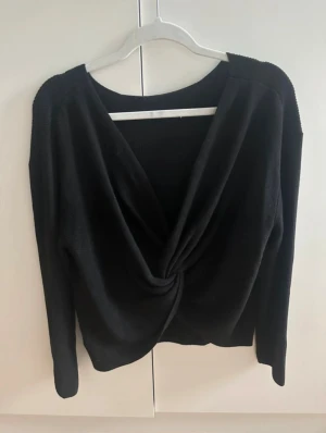 Svart stickad tröja med omlottdetalj i ryggen - Säljer en svart stickad tröja med snygg omlottdetalj i ryggen. Tröjan har ärm och en lite lösare passform. Perfekt för dig som gillar stilren men ändå trendig look. Passar till många olika outfits och är superenkel att matcha