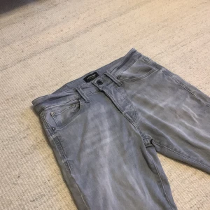 Grå slim jeans från Jack & Jones - Slim Glenn jeans från Jack & Jones i en snygg ljusgrå tvätt. Modellen har klassisk femficksdesign, smal passform och normal midja. Materialet är mjukt jeans-tyg med lite stretch för extra komfort. Perfekt för dig som gillar stilrena och moderna jeans.