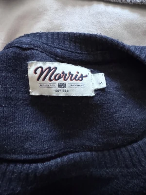 Mörkblå stickad tröja Morris M - Snygg mörkblå stickad tröja från Morris med rund hals och broderad logga på bröstet. Tröjan har långa ärmar och ribbade muddar vid ärmslut och nederkant. Perfekt för dig som gillar klassisk stil med en modern touch.