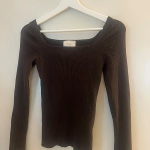Brun ribbad topp från Neo Noir - Säljer en brun långärmad topp från Neo Noir med ribbad struktur och fyrkantig halsringning. Modellen är tight och har en stilren, minimalistisk look som är enkel att matcha. Perfekt för dig som gillar basic med en twist.