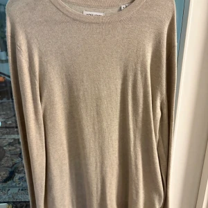 Beige stickad tröja Jack & Jones S - En stilren beige stickad tröja från Jack & Jones i storlek S. Tröjan har rund halsringning och långa ärmar, perfekt för lager-på-lager. Materialet är mjukt och lätt, vilket gör den skön att bära under höst och vår. Enkel design utan mönster eller detaljer. Den är helt ny använd en gång och helt felfri.