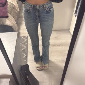 Blå bootcut jeans från Gina Tricot - Säljer ett par ljusblå bootcut jeans från Gina Tricot, modell perfect jeans. De har hög midja, klassisk femficksdesign och råa kanter med slits nertill. Jeansen är i ett mjukt bomullsmaterial och har en snygg tvättad look. Perfekta till sneakers eller boots.