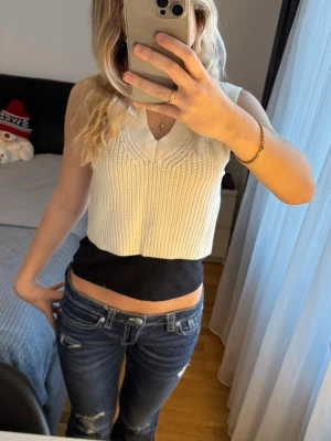 Vit croppad stickad väst från H&M - Säljer en vit croppad stickad väst från H&M i storlek S. Västen har en djup v-ringning och breda axelpartier, perfekt att styla över en t-shirt eller skjorta. Materialet är mjukt och ribbstickat för en trendig look.