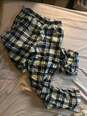 Blårutiga mjukisbyxor från H&M - Säljer ett par blårutiga mjukisbyxor från H&M med elastisk midja. Byxorna är tillverkade i mjuk bomull och har ett avslappnat snitt som passar perfekt för chill dagar hemma. Rutmönstret går i blått, vitt och svart.