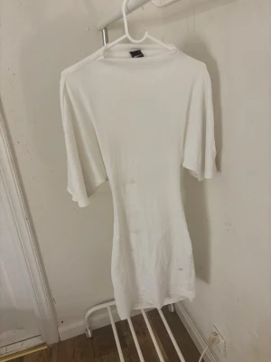 Vit kortklänning med knyt i ryggen - Säljer en vit kortklänning från GINA med rund hals och korta ärmar. Klänningen har en snygg öppen rygg med knytband som ger en cool detalj. Tillverkad i mjuk bomull som känns skön mot huden. Perfekt för dig som gillar enkel och stilren design.