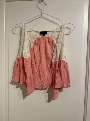 Mini rosa blus med spets  - Säljer en söt blus från Topshop i storlek S. Blusen har ljusrosa tyg med vida armhålor och vit spets upptill. Den har en luftig och flowy passform.