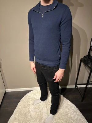 Blå half zip tröja från Jack & Jones - Mörkblå långärmad tröja från Jack & Jones i storlek XS men passar även M. Modellen är 178 cm o väger 75 kg. Tröjan har en stilren half zip-dragkedja vid kragen och är tillverkad i ett mjukt, stickat material. Perfekt för dig som gillar en clean och enkel look.