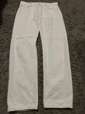 Vita relaxed jeans från J.Lindeberg - Säljer ett par vita jeans från J.Lindeberg med klassisk femficksdesign och relaxed passform. Byxorna har normal midja, bälteshällor och snygga detaljer i form av metallnitar och patch med logga bak. Perfekta till en clean och stilren look. 31/32