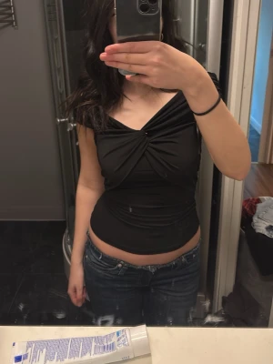 Svart omlott topp med snörning - Säljer en svart omlott topp med snygg snörning framtill. Toppen har offshoulder-design och är figurnära med en croppad passform. Materialet känns mjukt och stretchigt, perfekt för att styla med jeans eller kjol. Passar dig som gillar stilrena och trendiga plagg.