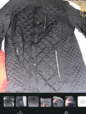 Rosetti Riding Svart quiltad jacka  - Quiltad svart jacka från Rosetti Riding med snygga dragkedjor och tryckknappar framtill. Jackan har ett coolt märke med hästmotiv på ärmen och är tillverkad i polyester. Perfekt för dig som gillar ridning och vill ha en stilren look. Sitter som en M