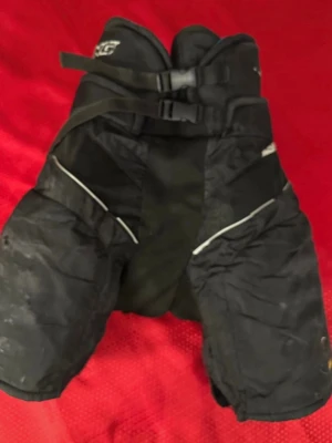 Svarta hockeybyxor Salming Vent M  - Säljer ett par svarta hockeybyxor Salming  med Vent Technology. Byxorna har två justerbara spännen framtill och meshpaneler för extra ventilation. De är vadderade och har vita detaljer längs sidorna. Perfekt för dig som spelar hockey och vill ha bra skydd och komfort. Det finns lite slitage, se bild. 