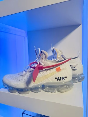 Off-White Nike Air Vapormax, Storlek 40,5 EU - Detta är ett par Off White Nike Air Vapormax köpta från stockX (2020-03/11) Se kvitto och orderbekräftelse.   Skorna är använda bara några gånger och sen bara stått på hyllan men fortfarande kritvita, det ända som förändrats är loggan som blivit lite gulare och yttre-air sulan pga older o material se bilder.  Off White zip-tie finns kvar även de extra blåa skosnören finns kvar, original sko-kartong och papper.