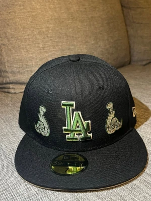 Svart LA Keps med design - Svart LA Keps med snygga designs på framsidan. Strl 55,8 men skulle säga att den är liten i storlek.