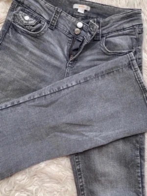 Grå jeans från Gina Tricot - Säljer ett par grå jeans från Gina Tricot i storlek 170. Jeansen har klassisk femficksmodell, två knappar i midjan och dragkedja. Materialet är mjukt denim och passformen är rak med normal midja. Perfekta till en avslappnad look.